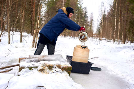 A man draws water from a spring in a plastic barrel in winter