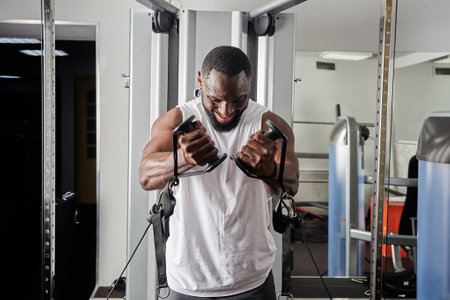 An African-American man is engaged in the gym on simulators.