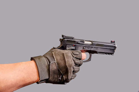 A mans hand holds a black pistol in his hand on a gray background