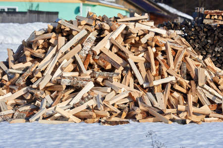 A pile of split firewood lies on the snow in winter
