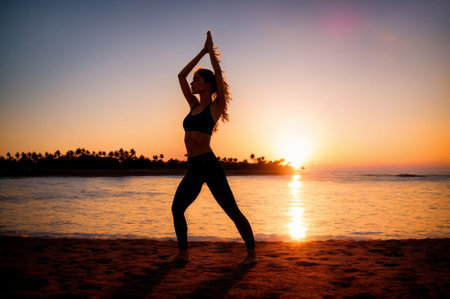 Silhouette of young woman practicing yoga on the beach at sunsetの素材