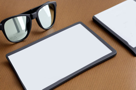 Tablet with blank screen and eyeglasses on wooden table.の素材