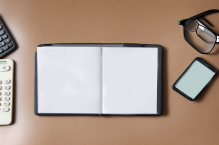 Top view of office desk table with blank notebook, smartphone, calculator and eyeglasses.の素材