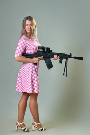 slender beautiful woman in a red dress with a machine gun in her hands on a gray background