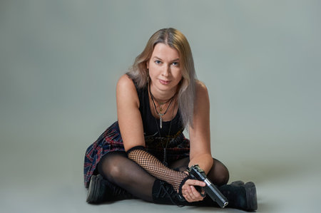 a beautiful woman with a gun in her hands is sitting on a gray background