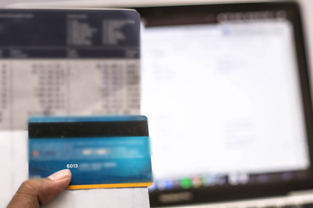 hand holding bank account book and atm credit card with laptop monitor as background