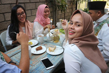 A young woman taking selfie while group of muslim people having diner and smiling during ramadan...