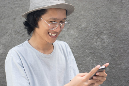 attractive young asian man with hat and glasses using smarphoneの写真素材