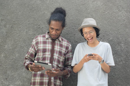 two man using smartphone, asian and black man best friend using smartphone and tabletの写真素材