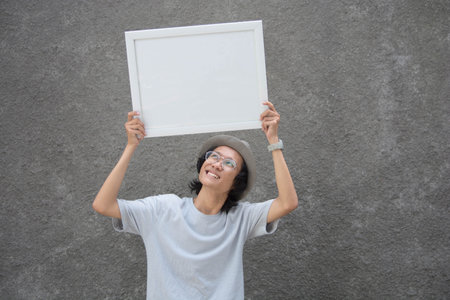 young asian student with glasses and fedora hat holding black board and smiling