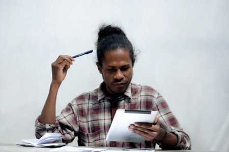 a young black man working and studying holding laptop and pen doing homeworkの写真素材