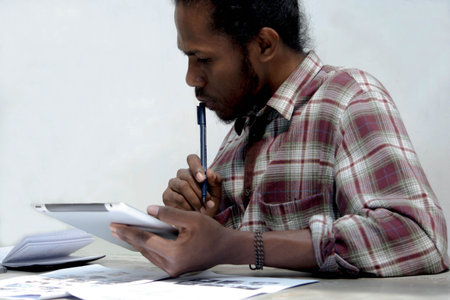 a young black man working and studying holding laptop and pen doing homework