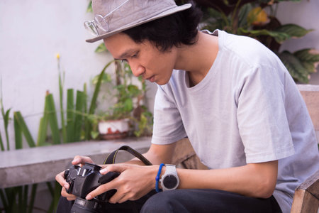 young asian man with hat and glasses holding and reviewing dslr camera