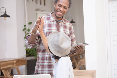 black man hand toast with a friend while holding a tablet or laptop, a man hand shake with friendの写真素材