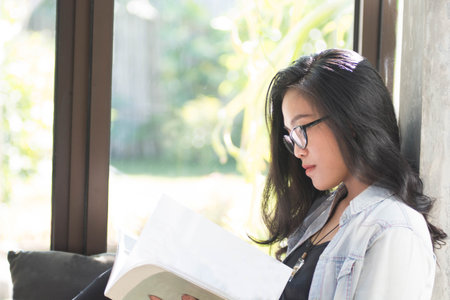close up of beautiful Asian women with glasses reading books while shiting by the window comfortably...