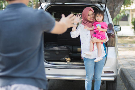 young muslim family , transport, leisure, road trip and people concept - happy woman and little girl waving at father to say goodbye and welcome beside car with trunk open and suitcase inside at outdoorsの写真素材