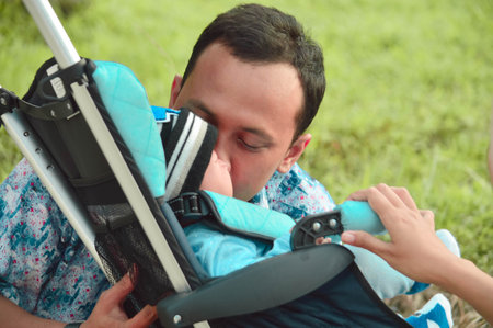 father walk through the park with son in stroller while kissing his son