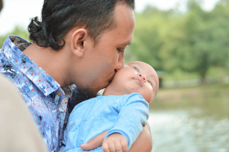 father walk through the park near lake with holding his todler while kissing his baby son