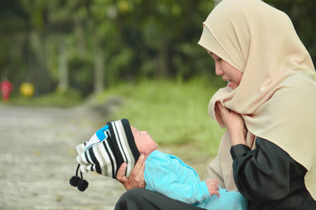 happy muslim hijab mother holding a beautifull baby while her todler crying in the outdoor area