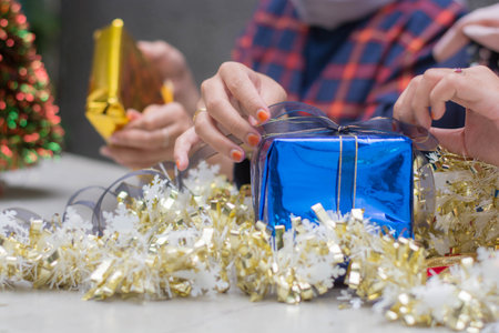 two woman s hands wrapping christmas gift, close up, unprepared chistmas presents on cement table at...