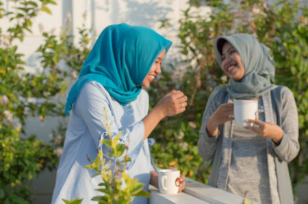 blurry portrait of two hijab  women drinking tea in front of the house and talking