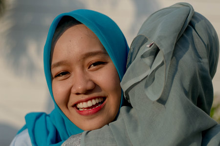 close up shot of two happy hijab women, smiling at the camera while hugging in front of their house...