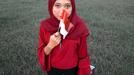 portrait of young asian muslim woman with scarf with small red and white flag into the air at sunset...
