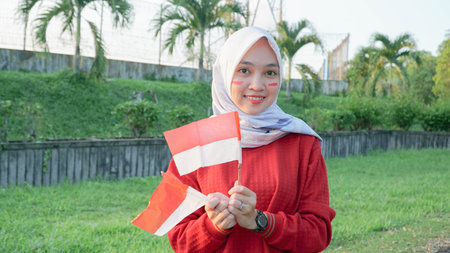 portrait of young asian muslim woman with scarf with small red and white flag into the air at sunset...