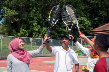 portrait group of people with young and old raise their rackets to the sky together for fair play before mixed double tennis match at outdoor hard court on day lightの写真素材