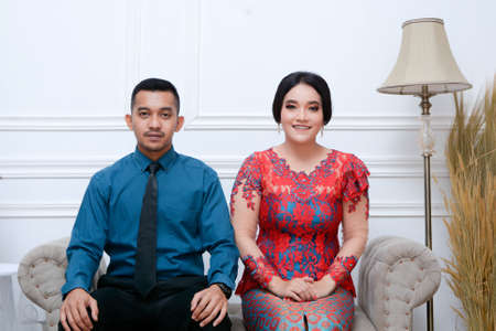 portrait of beautiful happy indonesian couple wearing traditional costume sitting on couch. batak...