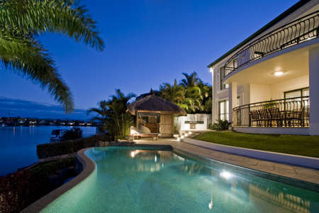 Luxurious mansion exterior at dusk overlooking pool, canal and Bali hut Luxurious mansion exterior at dusk overlooking pool, canal and Bali hut