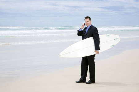 Business man in suit walking with surfboard on the beachの写真素材