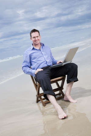 business man sitting on a chair on the beach with laptopの写真素材