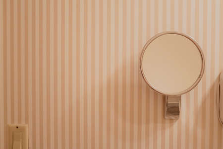 round mirror fixed to the wall of bathroom with peach striped wallpaperの写真素材