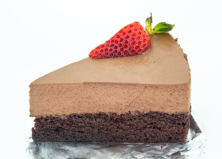 The piece of chocolate cake of two layers with fresh strawberries on foil and white backgroundの写真素材