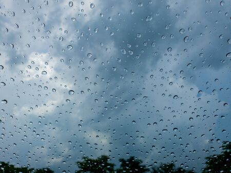 Wet window with rain drops and a cloudy stormy sky outsideの写真素材