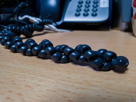 Black telephone wire on wooden table and blurred phone blackgroundの写真素材