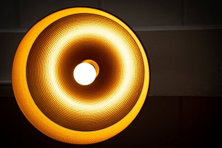 A Modern lamp hanging down from ceiling in the dark background. Minimalist chandelier with glowing warm light from bulb.の写真素材