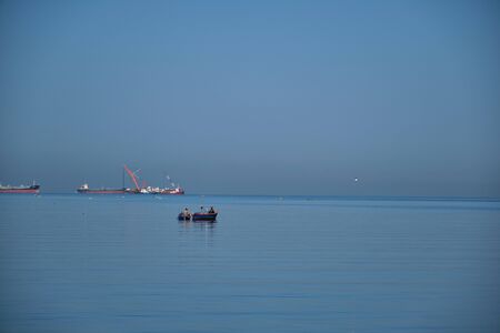 The Small Fisherman Boat in the Sea. A small fisherman boat floating on the sea near the seashore with Cargo ship backgroundの写真素材