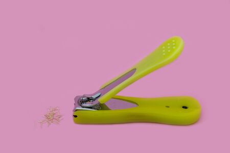 A Stainless Steel with green plastic handle Nail Clippers and some nails isolated on pink background.の写真素材