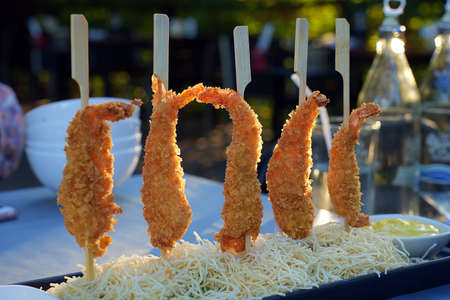 Shrimp in batter with fried potatoes and sauce on a wooden tray. Closeup