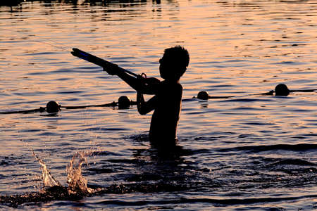 Sunset silhouette of happy child enjoys water games in the poolの写真素材