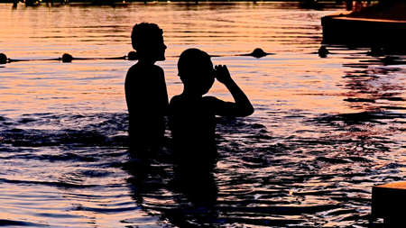 Sunset silhouette of happy children enjoy water games in the pool