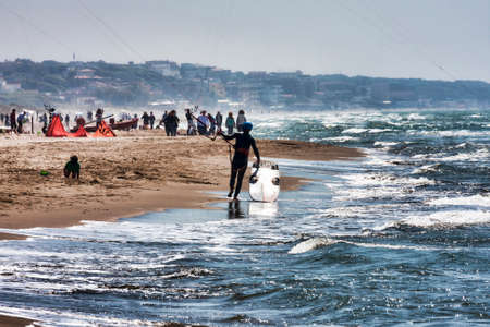 Lido dei Pini, Italy - April 25,2014: On the Roman beach of Lido dei Pini an athlete walks on the shore with his surfboard between waves and foam, a perfect day with the wind and rough sea necessary for this sport.のeditorial素材