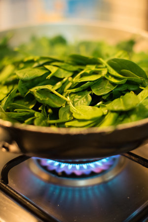 Fresh green spinach leaves in a frying pan on a gas stove.