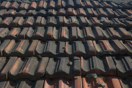 Roof tiles. Weathered, aged old faded dirty tiles on the roof of a house, creating an uneven texture.の写真素材