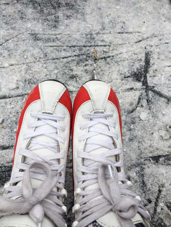 A pair of feet in women's skate lace-up boots, in white and red, close-up, against the scratched...