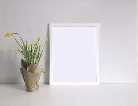 White frame template for a photo or picture in the interior with a bouquet of daffodils
