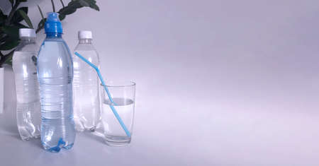 Plastic bottles and a glass with clean water and a cocktail tube on a gray background. There is a...