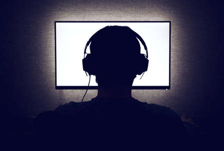Man in headphones sits in front of a blank monitor in dark roomの写真素材